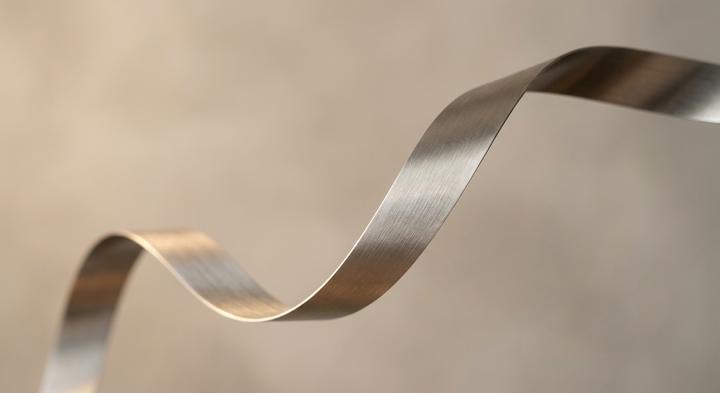 Minimalist abstract view of curved metal strip representing stress relief and material flow